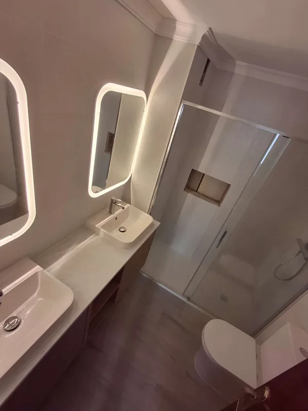 Baño reformado con lavabo suspendido, espejo LED y ducha con mampara — Junior Reformas