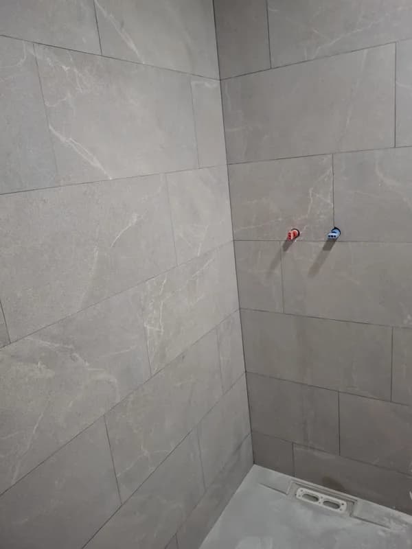 Ducha alicatada en gris con tomas de fontanería preparadas para grifería — Junior Reformas
