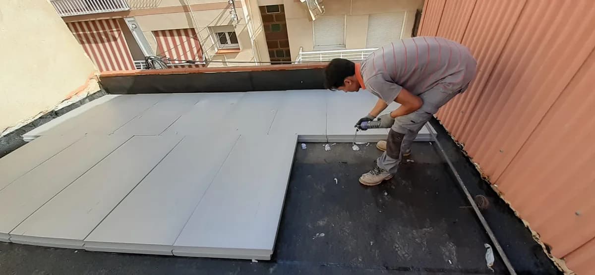Exterior en curso: trabajador instalando aislamiento tejado — Junior Reformas
