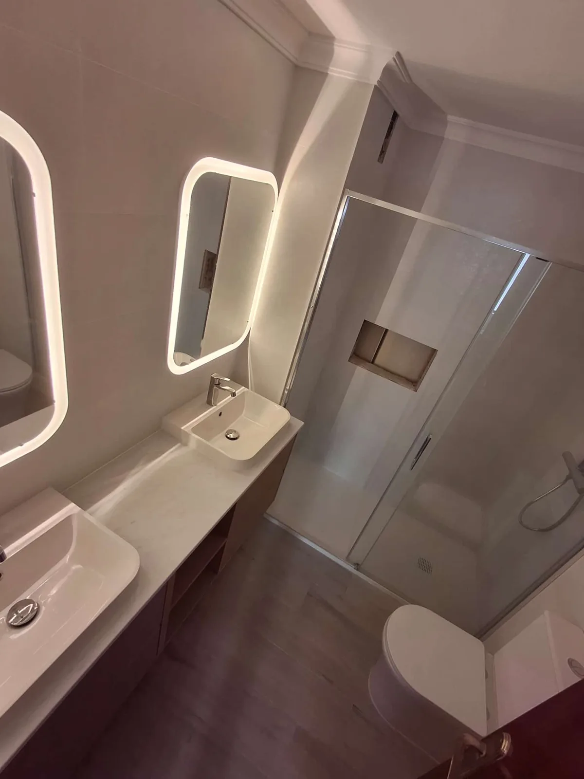 Baño reformado con lavabo suspendido, espejo LED y ducha con mampara — Junior Reformas