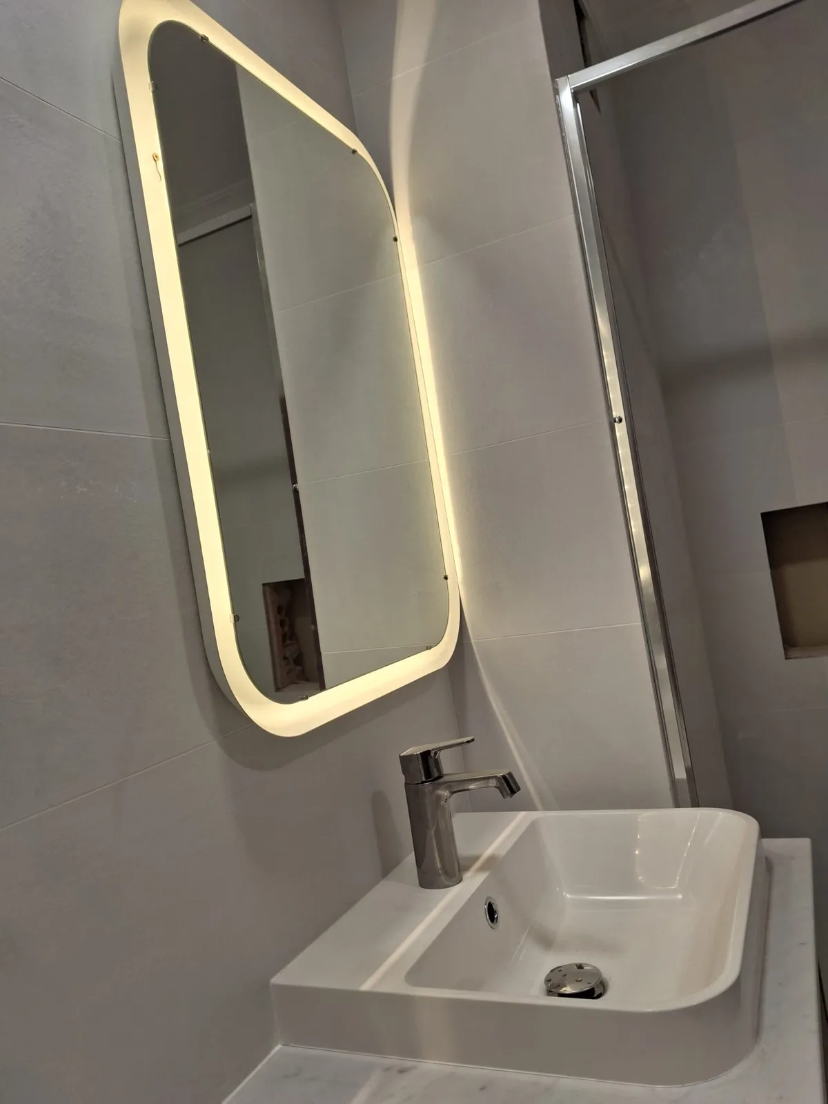Zona de lavabo con espejo LED y grifería moderna en baño reformado — Junior Reformas
