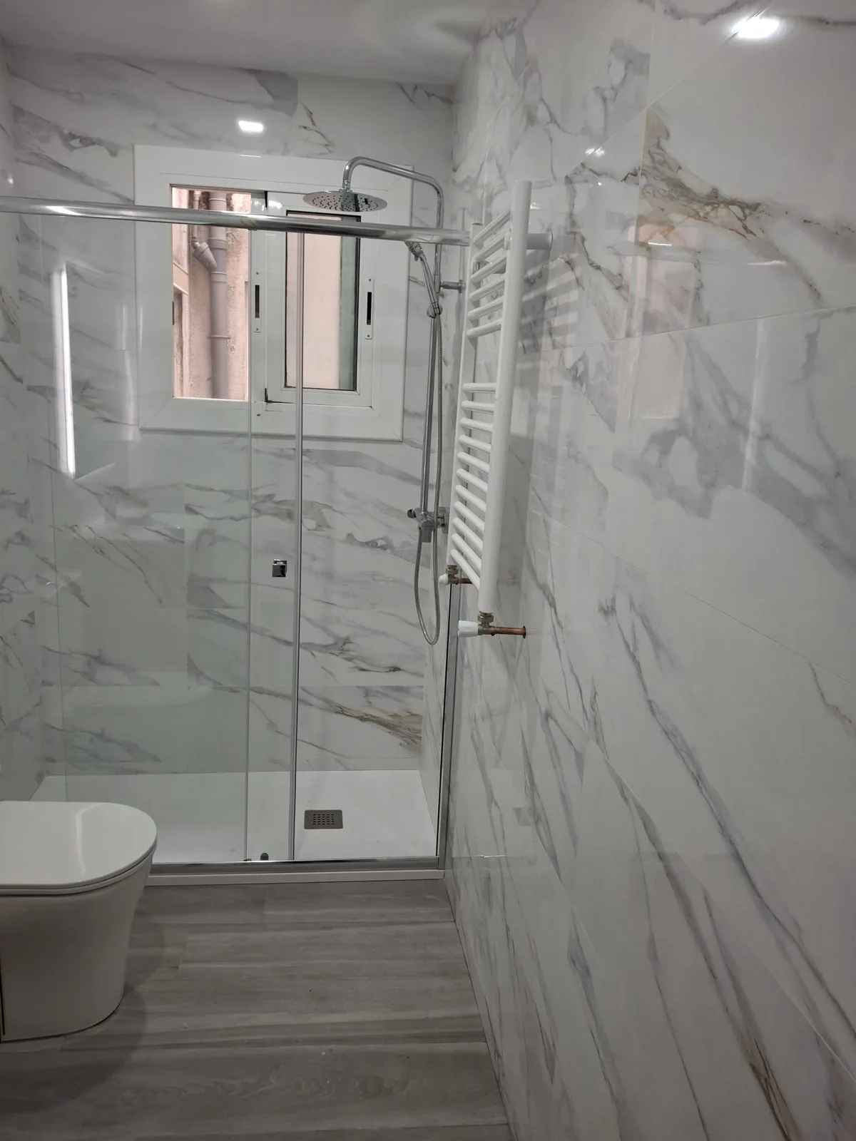 Baño reformado con azulejos efecto mármol, plato de ducha a ras de suelo y mampara de cristal — Junior Reformas